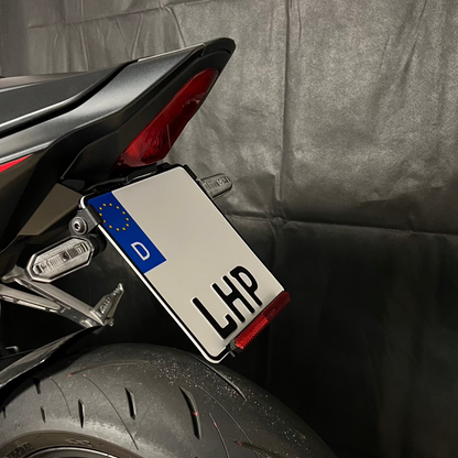 Kurzer, klappbarer Kennzeichenhalter für Honda CB / CBR 650R 2024 aus 3 mm starkem Aluminium, schwarz pulverbeschichtet, mit stufenlos verstellbarem Kennzeichenwinkel und Adapter für originale Blinker.